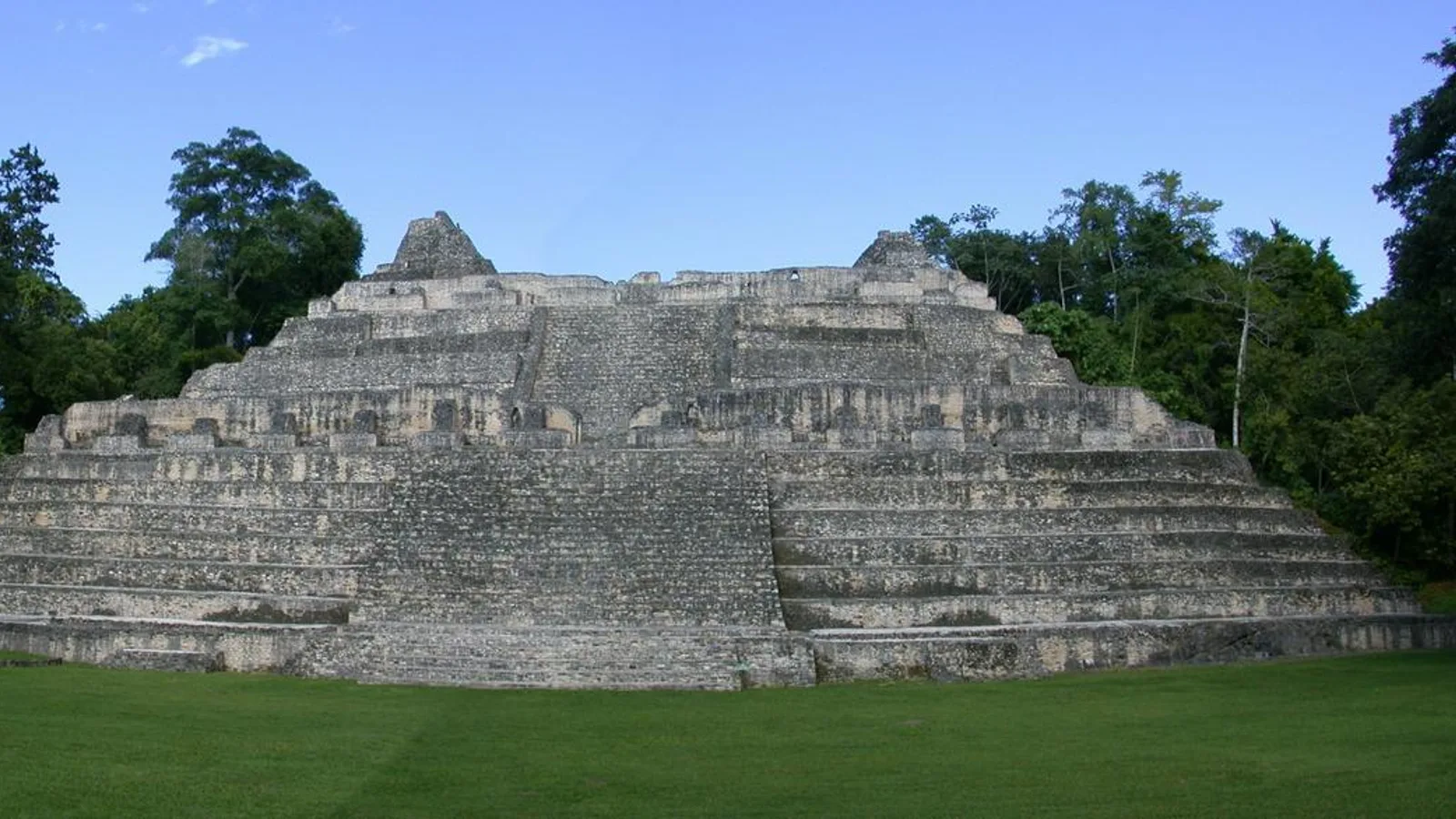 The stepped Caana palace complex rising above a grassy plaza at the Caracol Maya site in Belize, surrounded by jungle